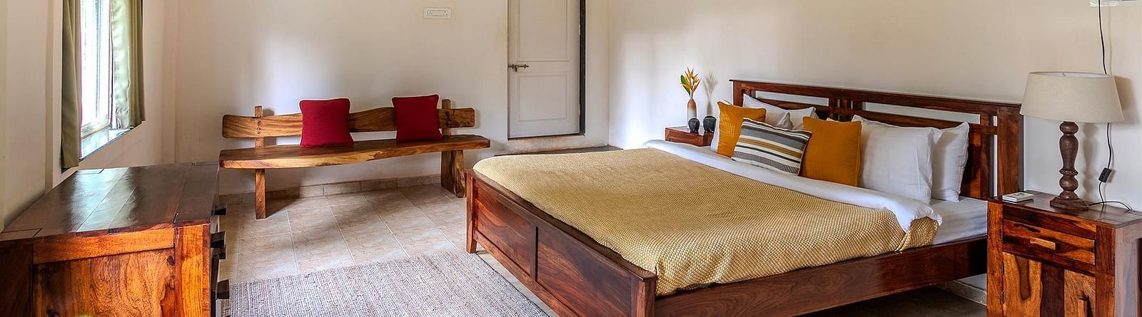 A double bed room with side table, lamp, a desk, seating bench, ceiling fan, AC and a door The Conservancy Bungalow