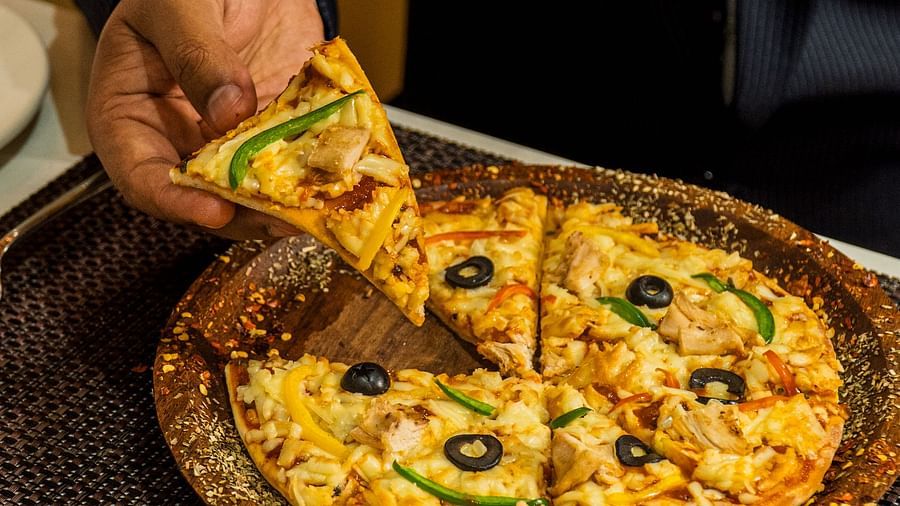 Person serving a slice of pizza topped with vegetables and olives.