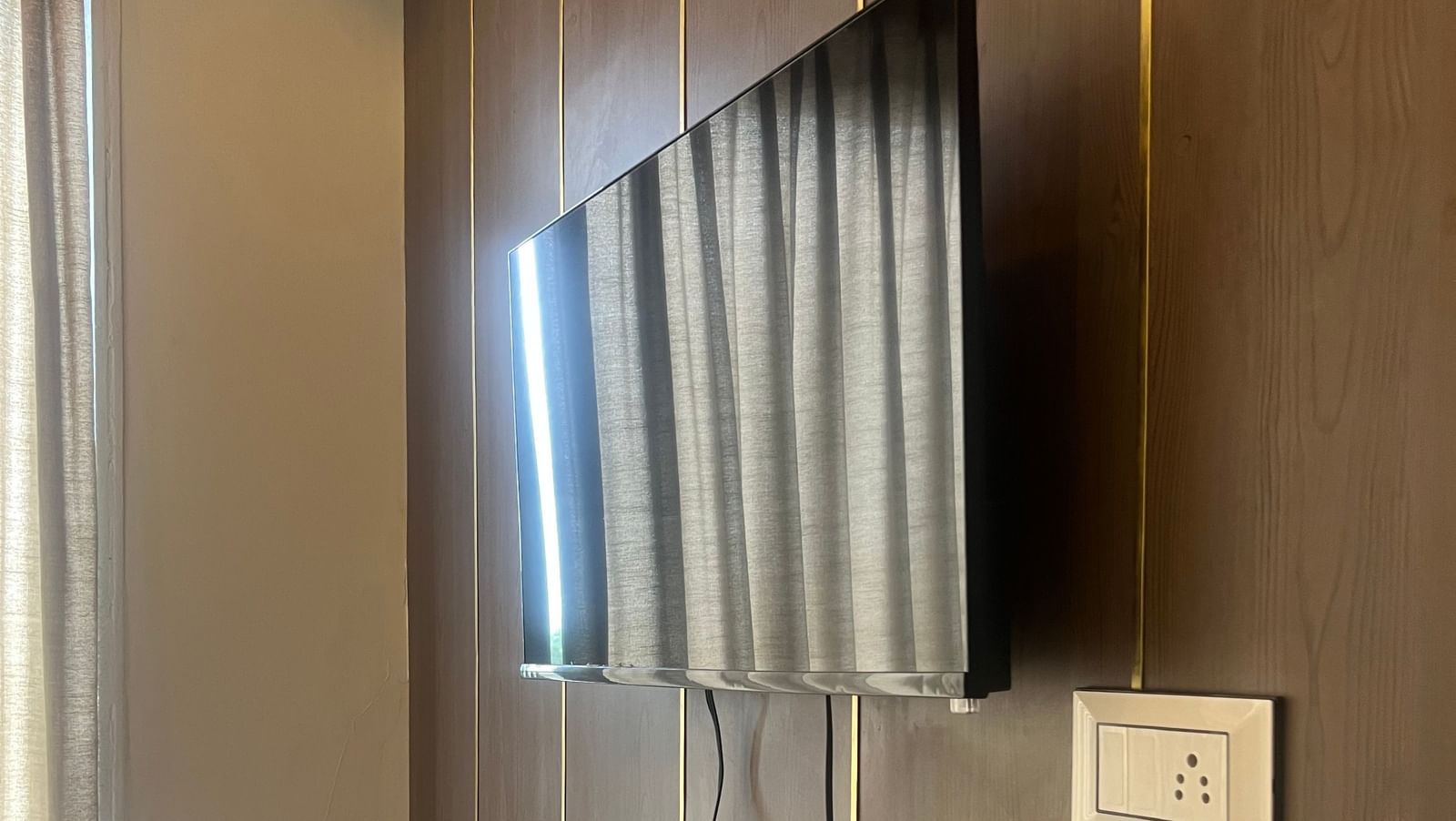 Wall-mounted TV in a Daksh Comfort Room at Daksh The Valley Resort, Saputara, with a wooden shelf below.