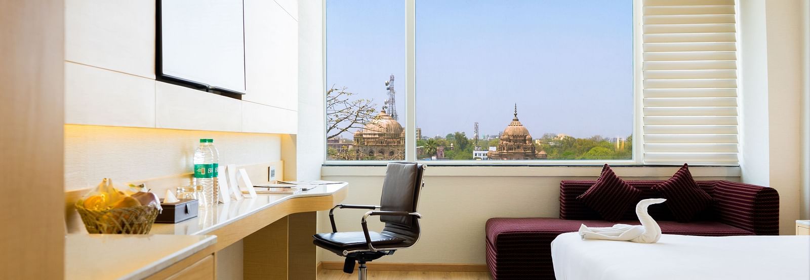 Brightly lit hotel room in Lucknow with a large bed, workspace, and a heritage window view | Gemini Continental