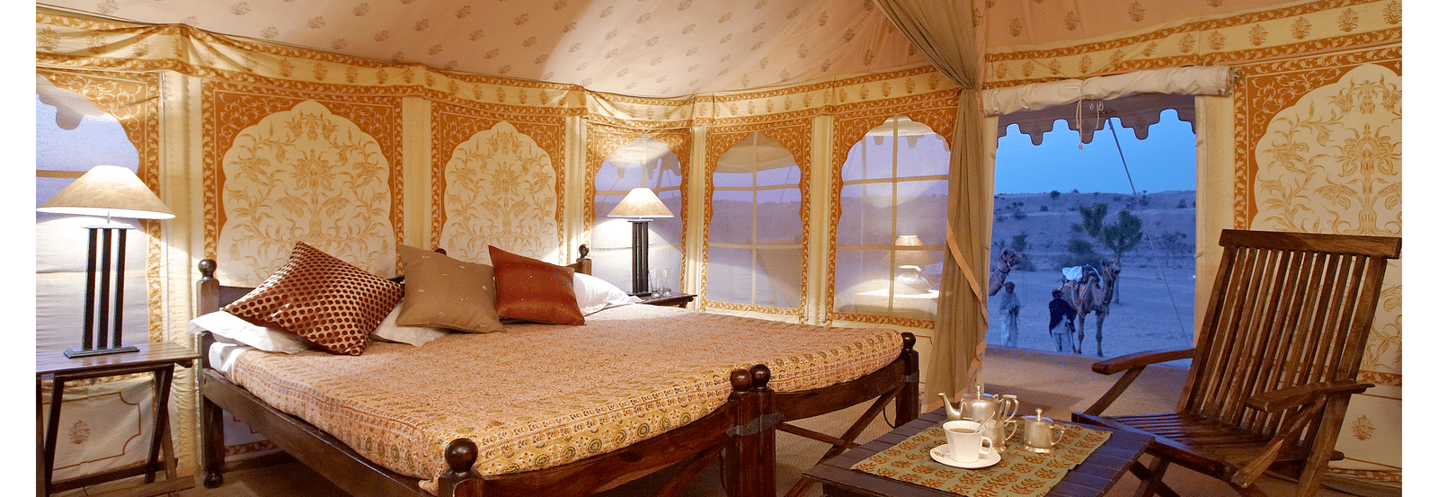 A tent style room with a double bed, carpeted floor and rocking wooden chair at MANVAR Sevan The Desert Camp.