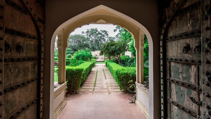 An arched doorway offering a view of a long, hedged pathway leading away from Royal Heritage Haveli.
