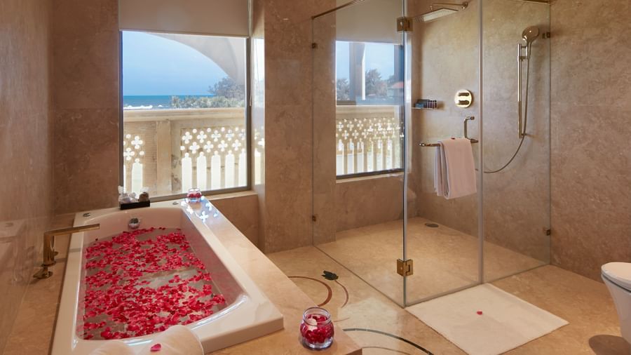 A luxurious bathroom with a petal-decorated bathtub and large glass shower enclosure - Kaldan Samudhra