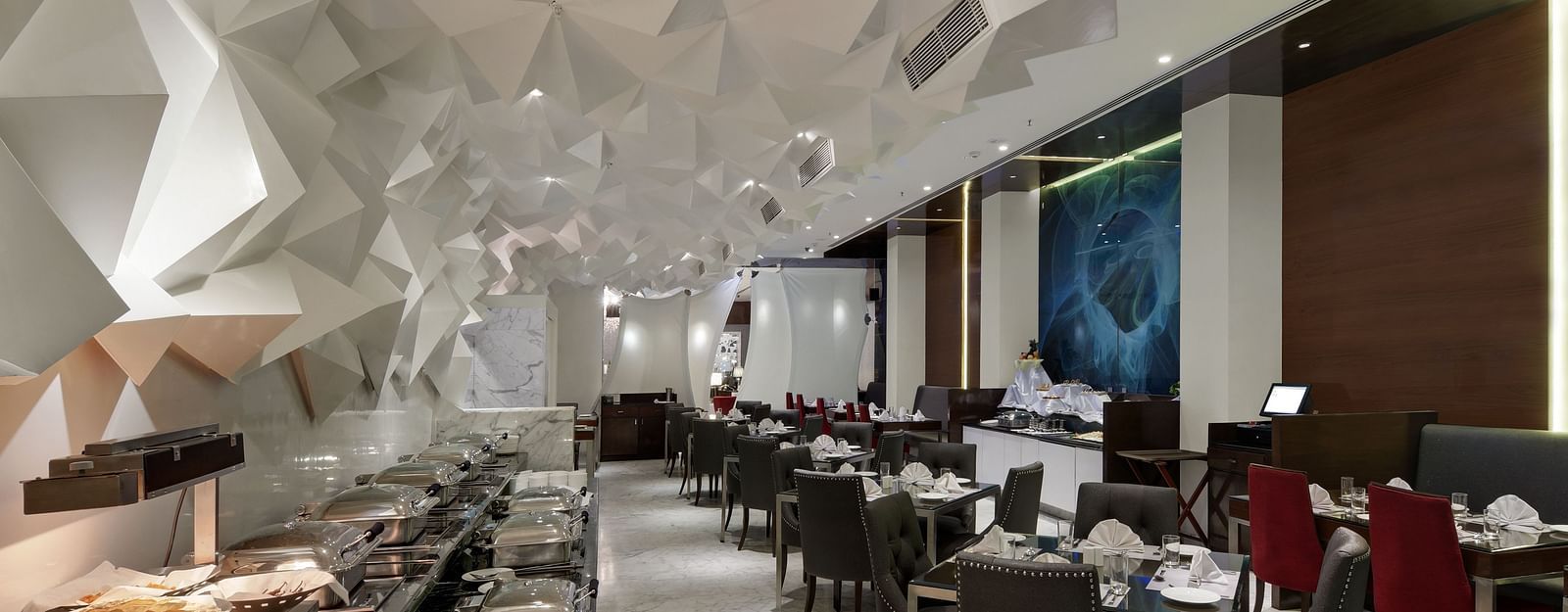 Modern indoor dining area with elegant seating, buffet setup, and artistic geometric ceiling decor