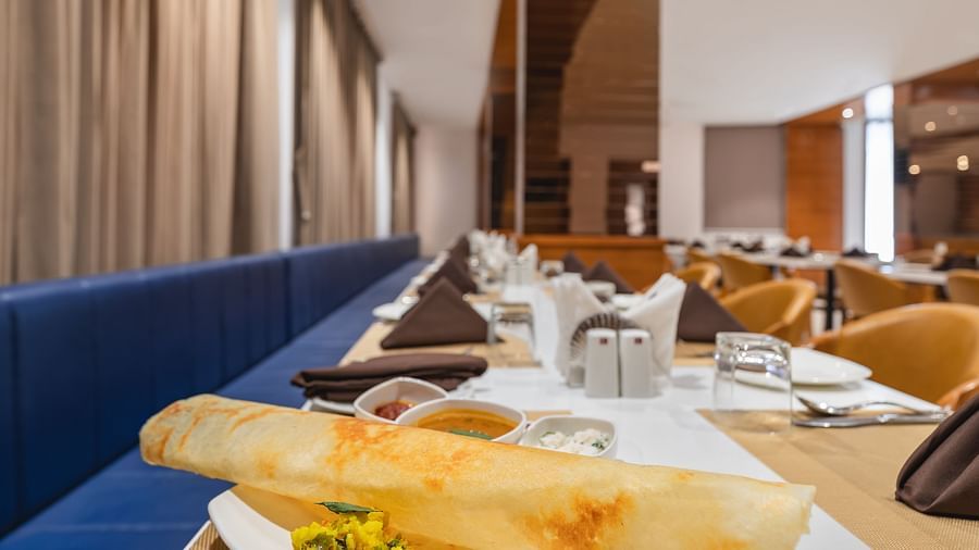 A long, thin crepe with a side of filling sits on a plate on a set table in a restaurant - Lords Eco Inn Ambaji.