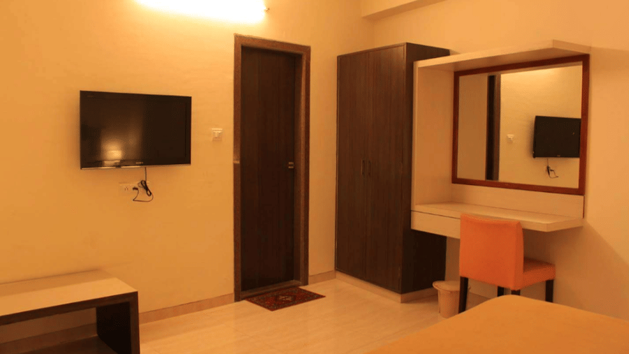 deluxe room showing a bed corner, wall-mounted television, and a dark wooden bathroom door.