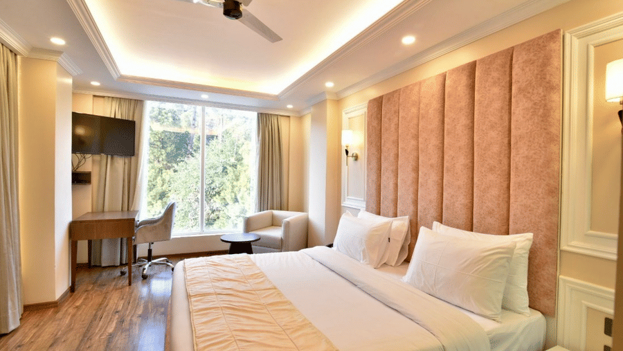 Spacious hotel room with queen size bed, padded headboard, and serene hill views at Claret Inn, Dalhousie.
