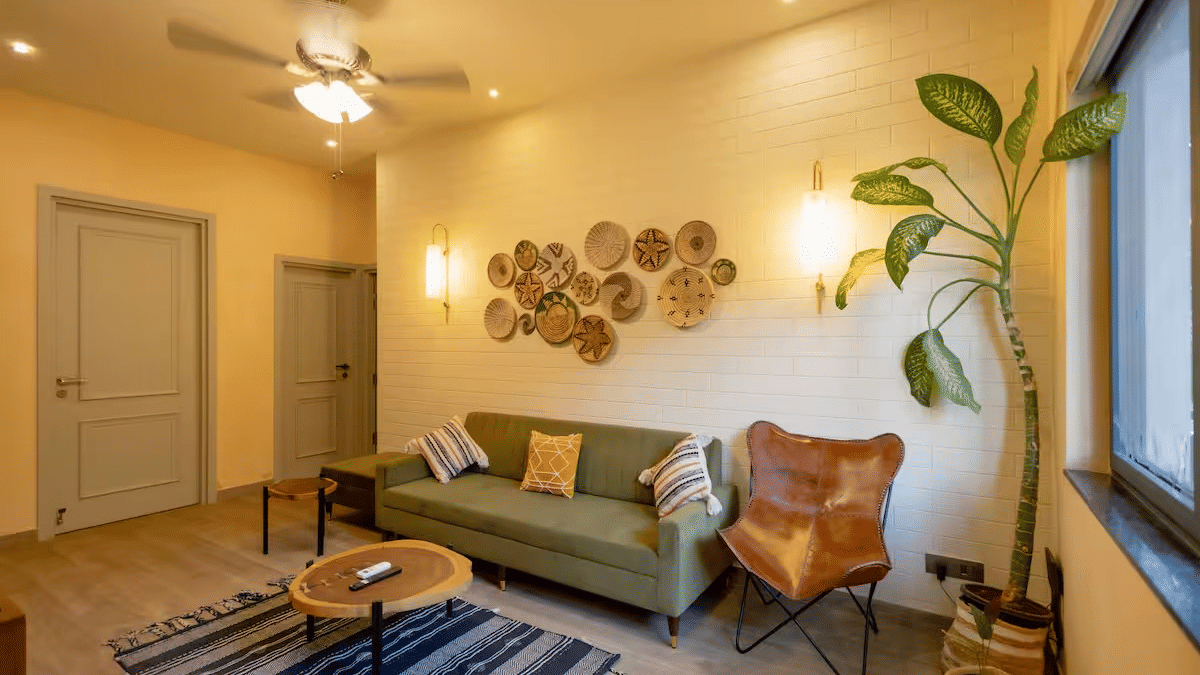 Living room of Lime Tree Hotels & Service Apartment Private Limited featuring a grey sofa, a potted plant, and circular wall art above the seating area.