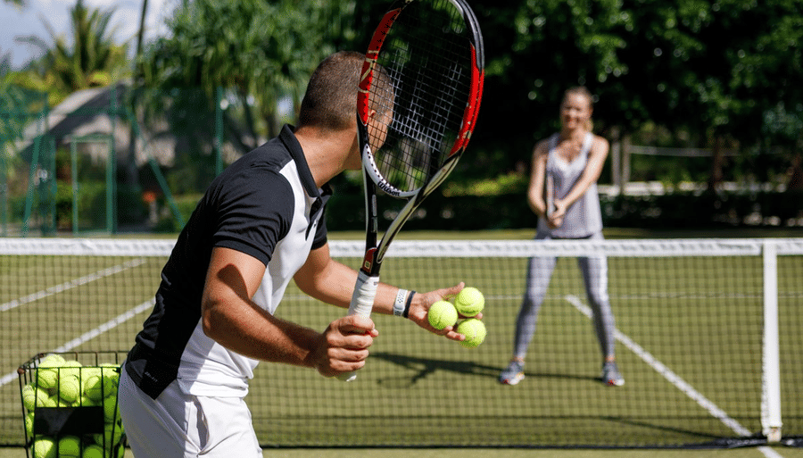 a person holding three tennis balls and another waiting to receive the balls 