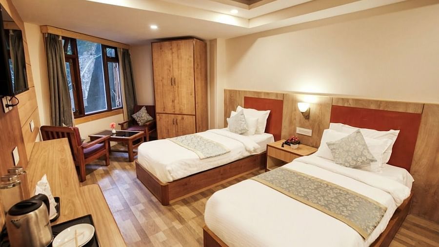 Standard Twin Room at Avianna Gangtok Prime Hotel & Spa featuring a couple of twin beds facing the TV mounted on the wall below which is tea and coffee maker. On one side of the bed is a sitting space next to the window