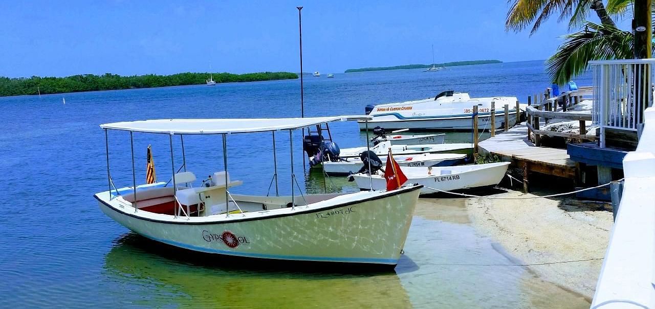 Boats moored on the shore at Casa Morada with clear skies, palm trees, and calm sea in the background.