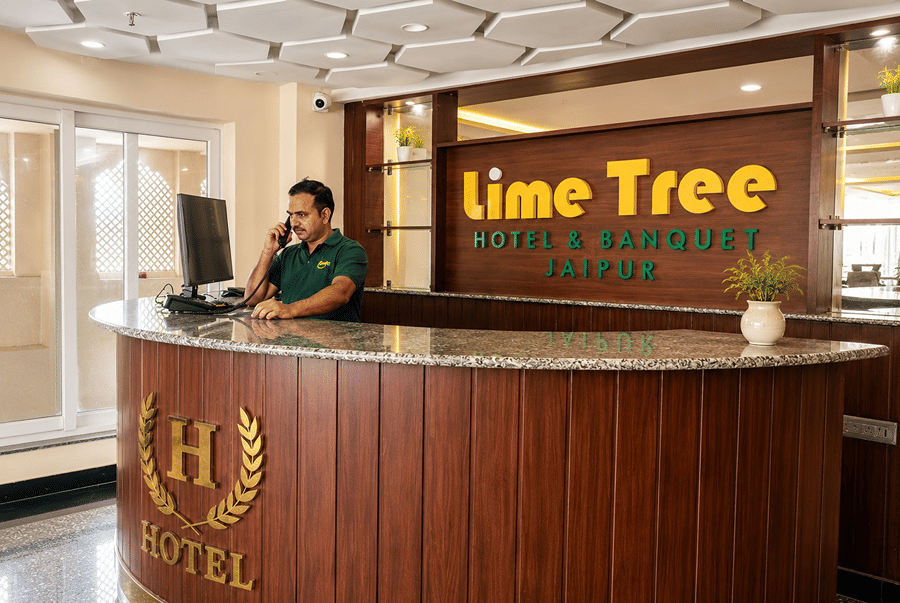 Receptionist on the phone behind the wooden front desk in the lobby of Lime Tree Hotel & Banquet, Jaipur