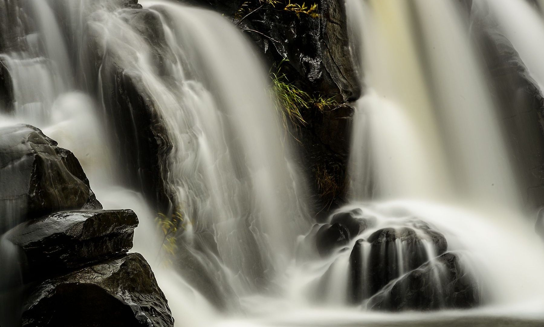 Long exposure of serene Coorg waterfall over dark rocks.