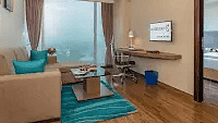 A bright area with a couch and cushions on it under a colorful carpet and a unique chair beside it. - Golden Suites, Gurgaon