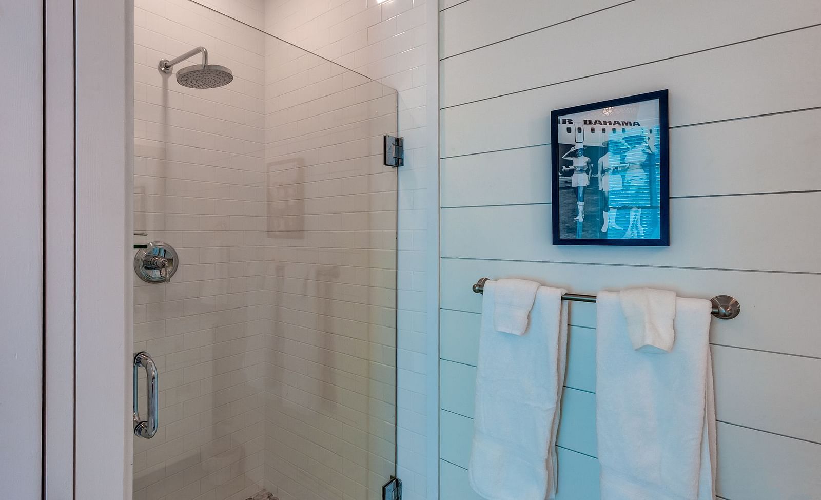 Bathroom with a glass shower enclosure, white towels, and framed wall art | Abaco Inn