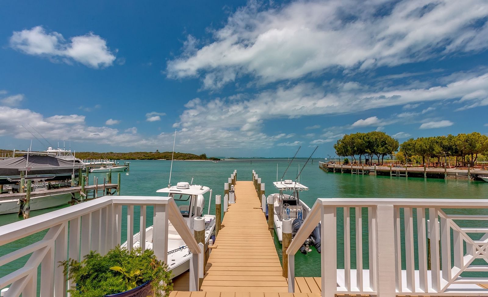 Boardwalk extending over water with white railings, leading to a dock with boats | Abaco Inn