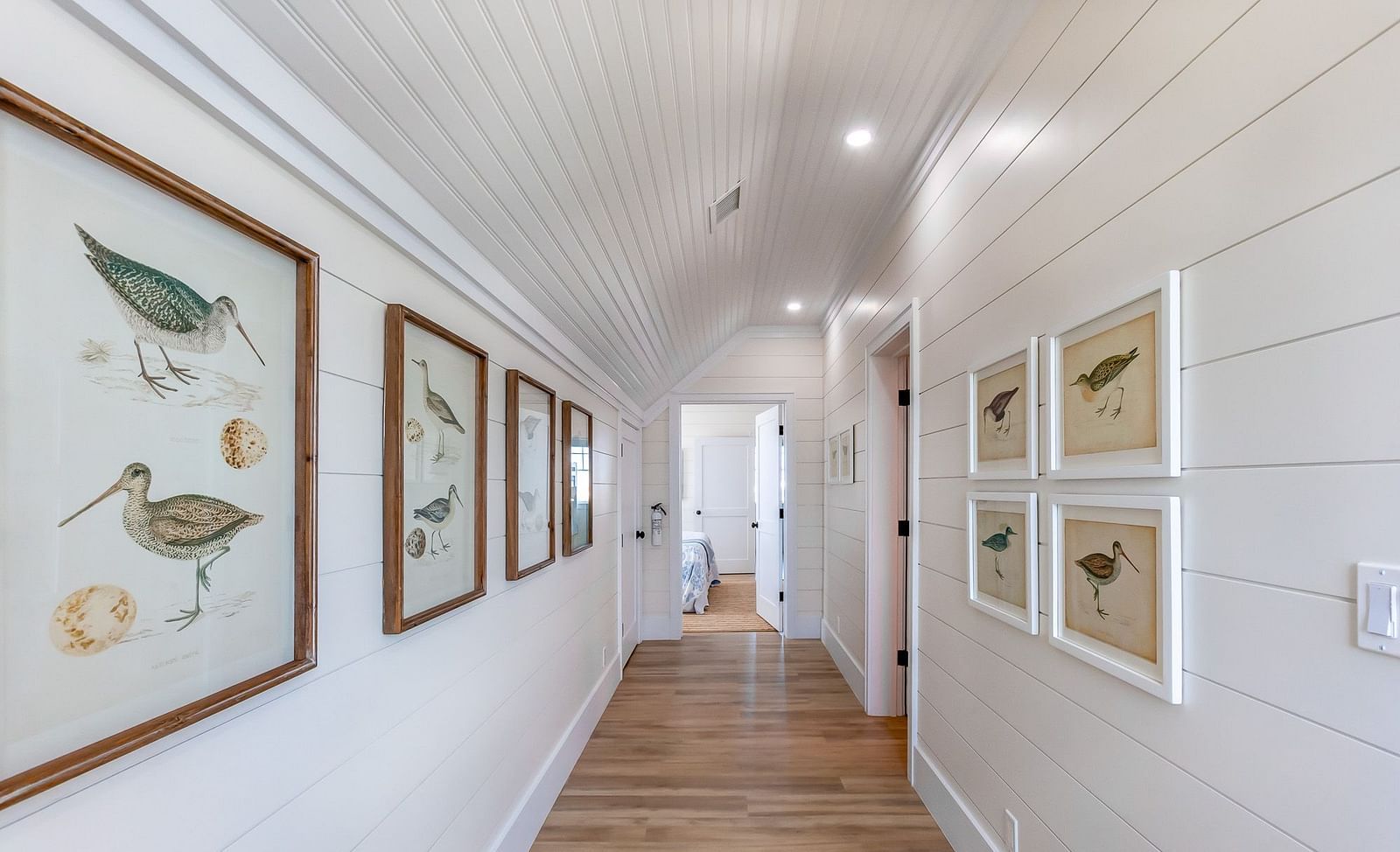 a corridor with wooden floor and white walls with paintings at Abaco Inn.