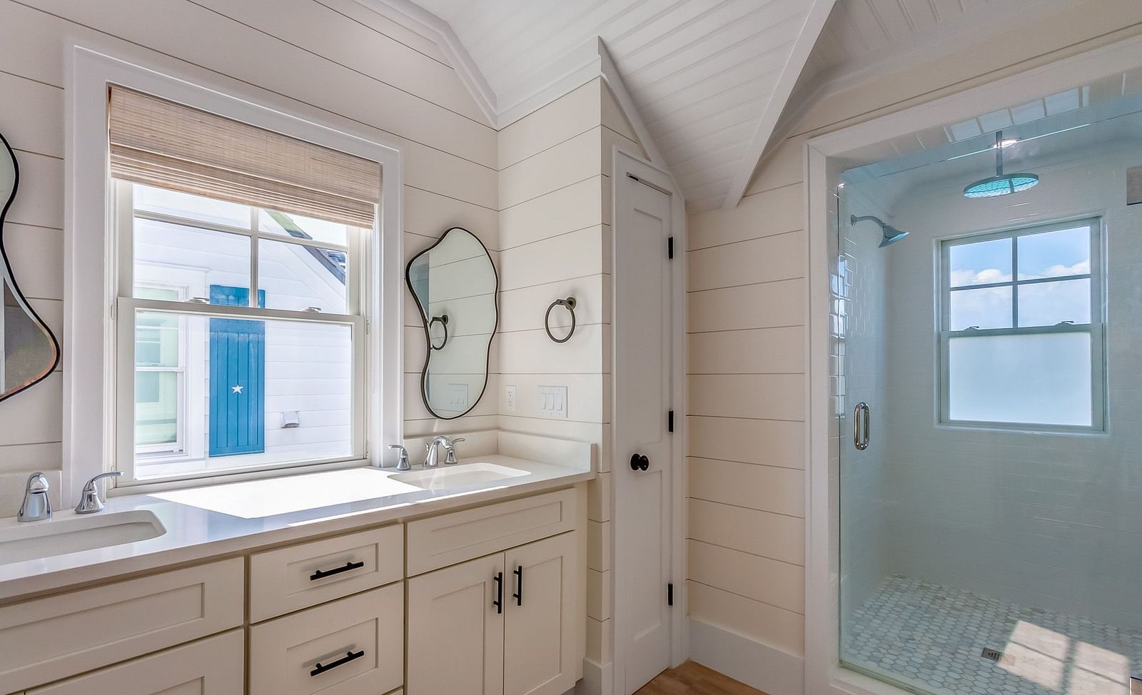 bathroom at abaco inn with cupboards, sinks, mirrors,  walk in shower, and windows .