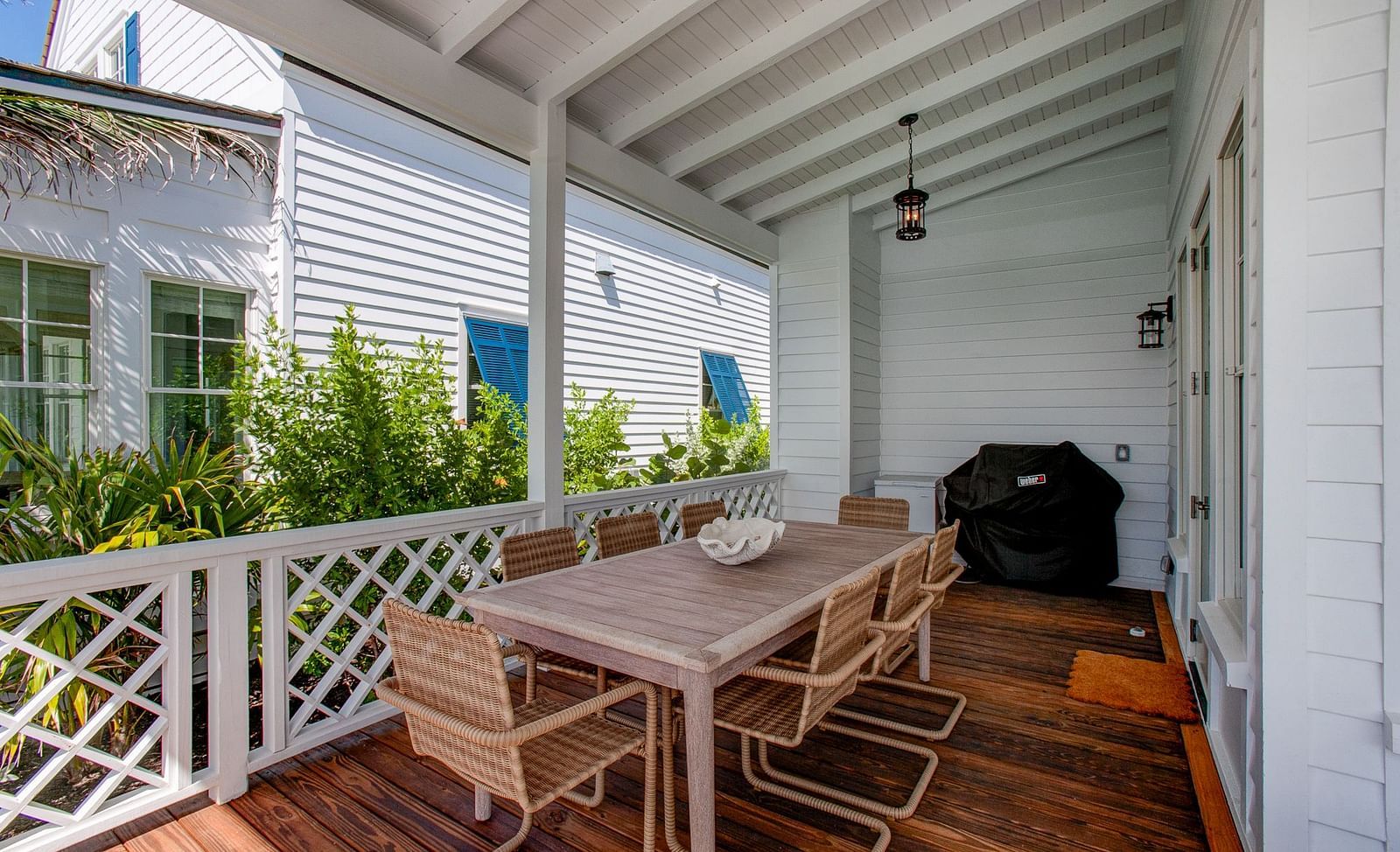 A spacious outdoor porch Abaco Inn featuring a dining table and chairs, a grill, and a railing, offering a view of nearby structures 