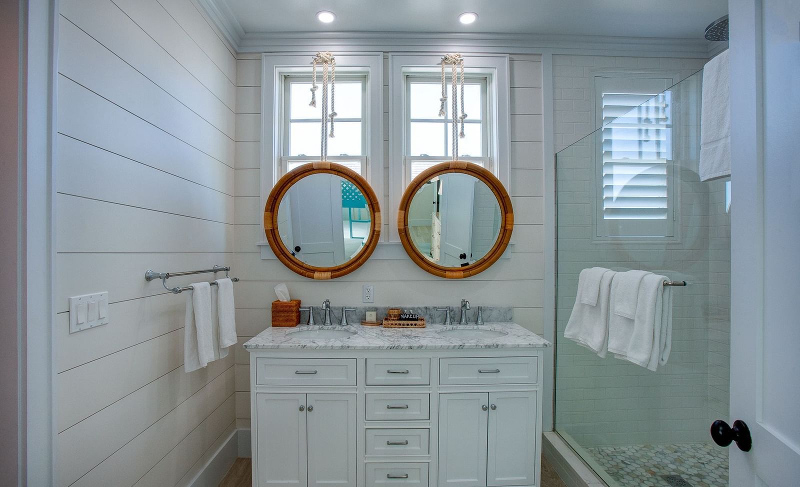 A well-lit bathroom at Abaco Inn featuring a vanity, two circular mirrors, and a shower enclosure, featuring walls composed of horizontal panels 