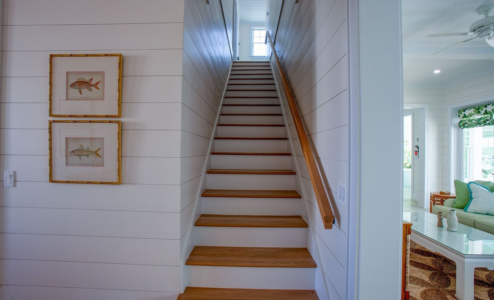An indoor staircase with wooden treads and risers at Abaco Inn, featuring framed artworks on the adjacent wall, leading upwards and out of view