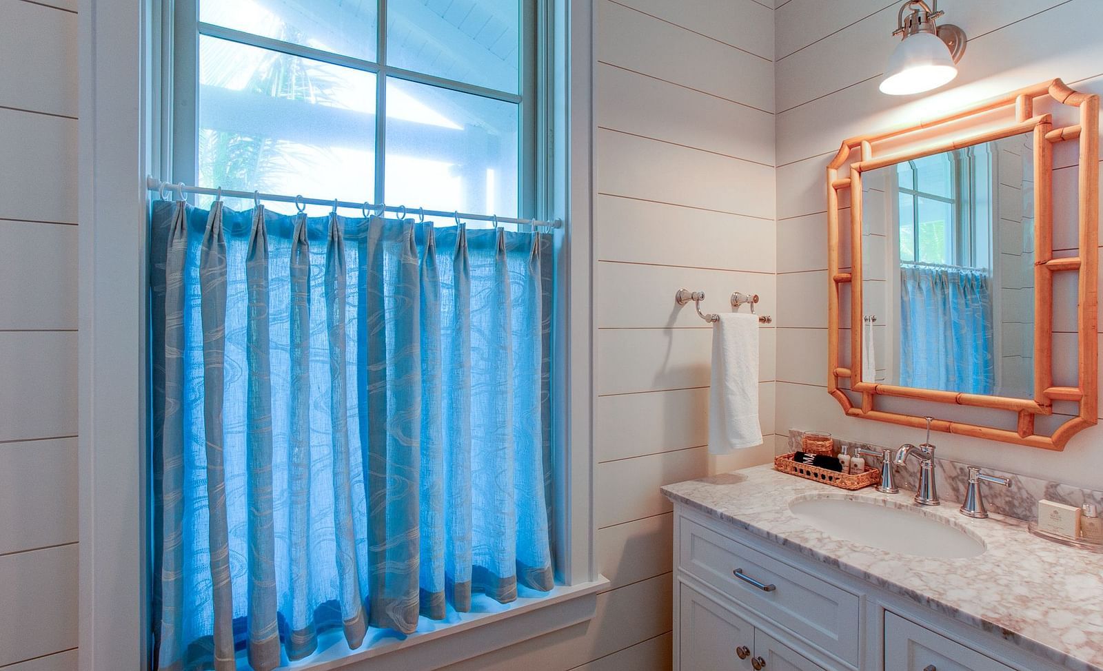 A bathroom interior at Abaco Inn showcasing a vanity with a counter and sink, a mirror in a substantial frame, and a window adorned with drapes