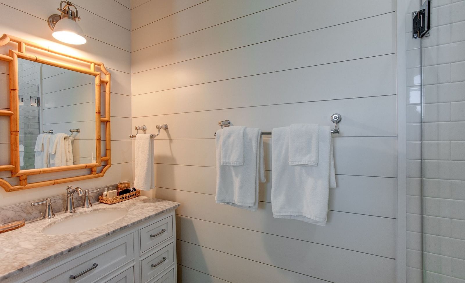 A bathroom interior at Abaco Inn featuring a vanity, sink, and a decorative mirror on a wall composed of horizontal panels, with folded linens hanging nearby 