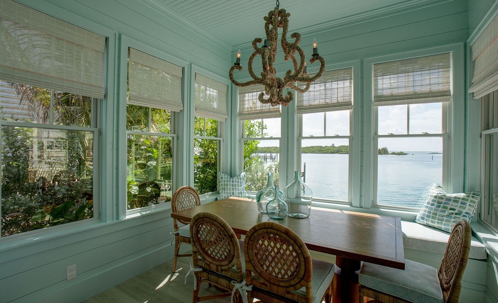 An elegant dining area with a large, ornate chandelier suspended above a wooden table surrounded by chairs, set within a room with numerous windows at Abaco Inn