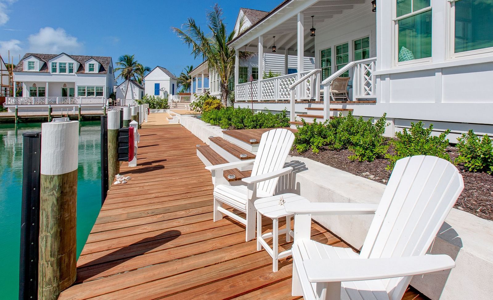 A wooden pier extending over water at Abaco Inn, featuring a set of lounge chairs and views of a cluster of waterfront houses under a bright sky