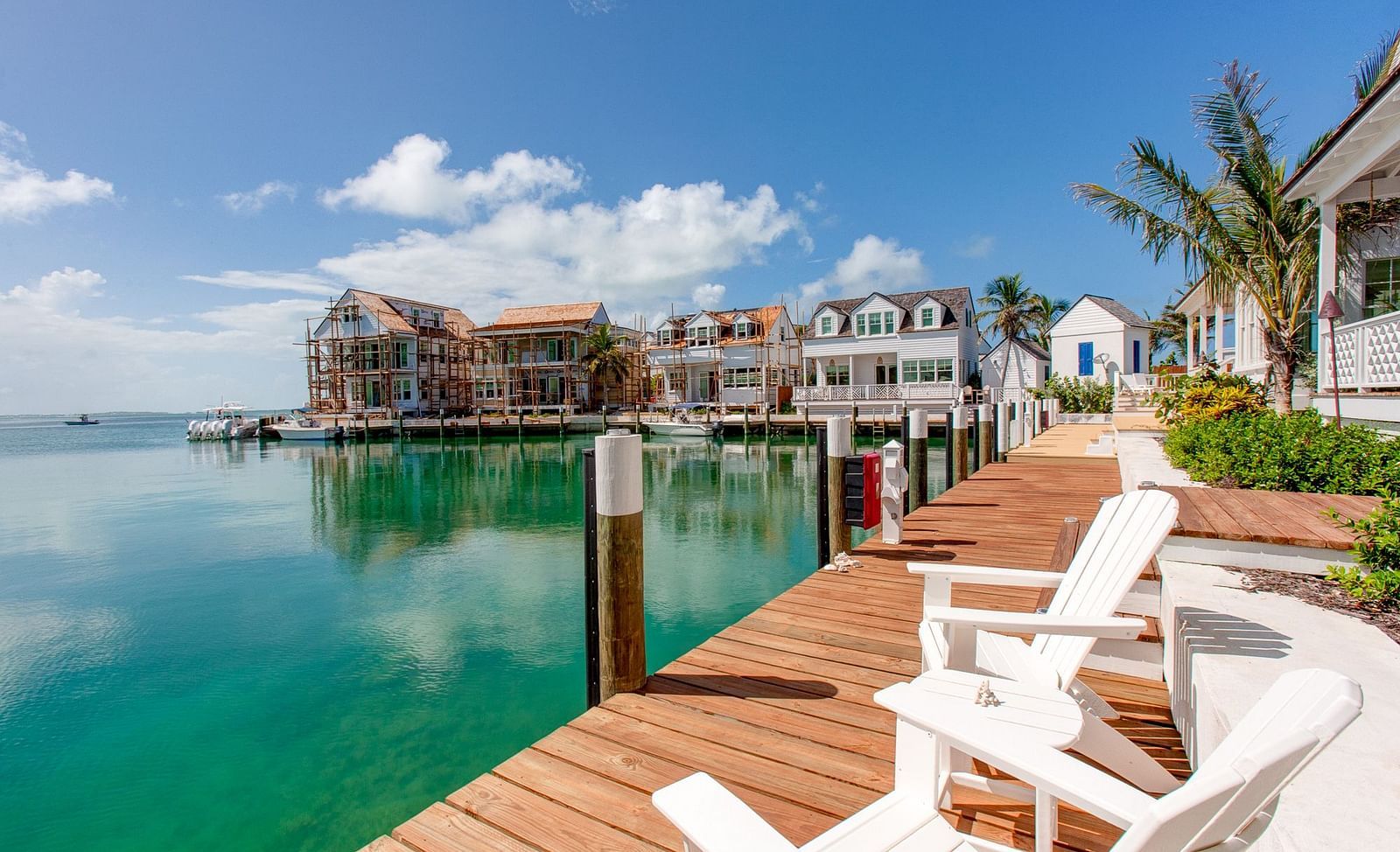 A wooden dock extending into a calm body of water, with several lounge chairs positioned to face a collection of waterfront houses under a clear sky at Abaco Inn