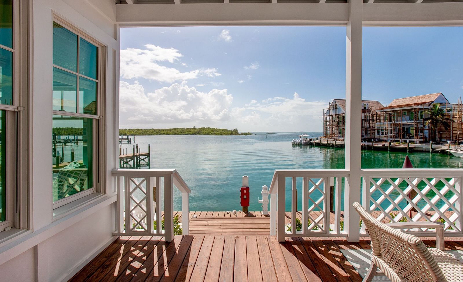 A waterfront porch Abaco Inn featuring a wooden deck and railing, overlooking a body of water with distant buildings under a clear sky