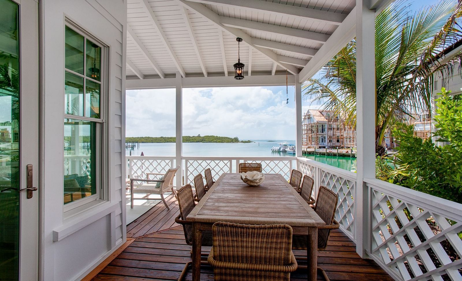 An outdoor dining area on a covered porch at Abaco Inn, featuring a long wooden table and chairs, with a view of a body of water and distant buildings