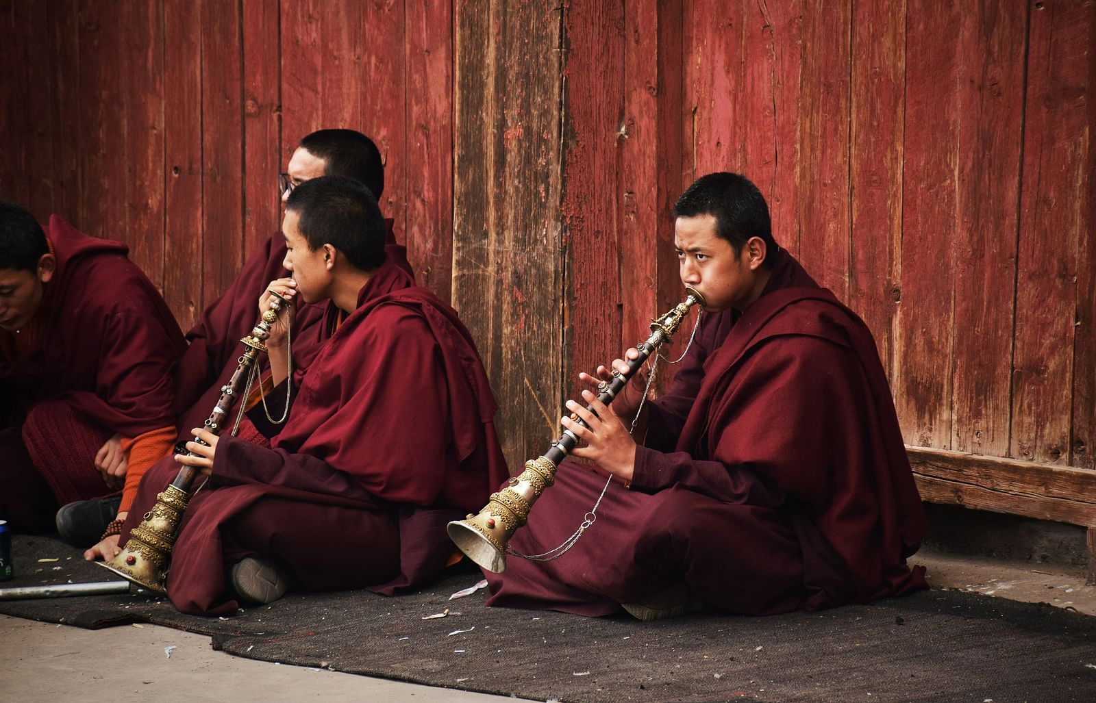 An image monks sitting on the ground and among them two monks are playing musical instruments