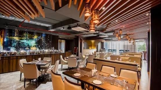 A restaurant with a fancy table setting for four and six and a buffet system towards the side, along with fancy ceiling lights at Yashshree The Imperial Inn, Siliguri.