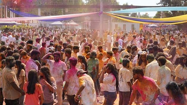 Holi festival-goers throwing colours in the air, surrounded by vibrant decorations and festive music.