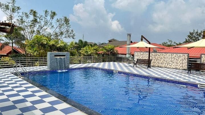 A clear blue swimming pool at Woodstock Resorts, Coorg with a view of the resort's landscaping.