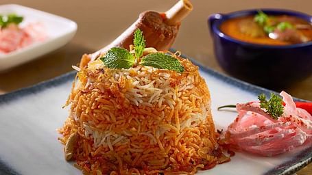 Plate of biryani served with raita and a side of curry in bowls.