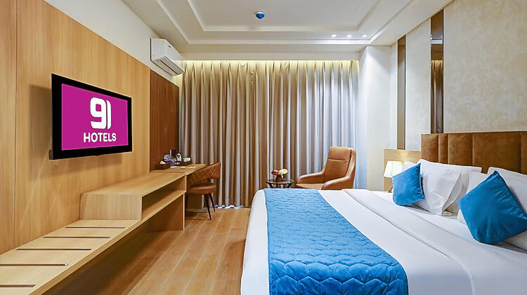 A bedroom at Hotel 91 HUDA Premier, Gurugram with a king size bed, pillows, wall-mounted TV, desk, chair, and armchair.