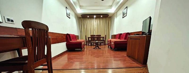 The living room of the Suite featuring a shiny wooden flooring along with red coloured couch set in the end - Hotel Gold, Panipat