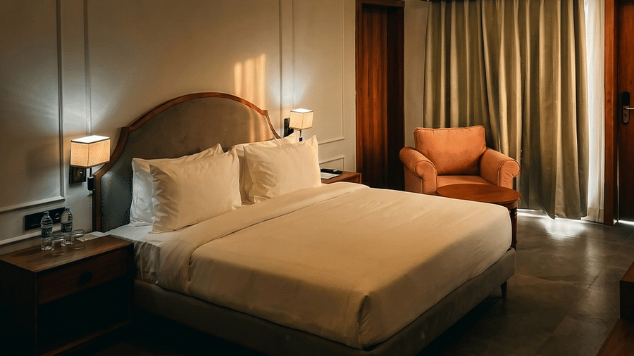 Bedroom featuring king size bed with white linens, wooden side tables, armchair, ceiling fan, and hanging chandeliers at Jivana Wellness Retreat.
