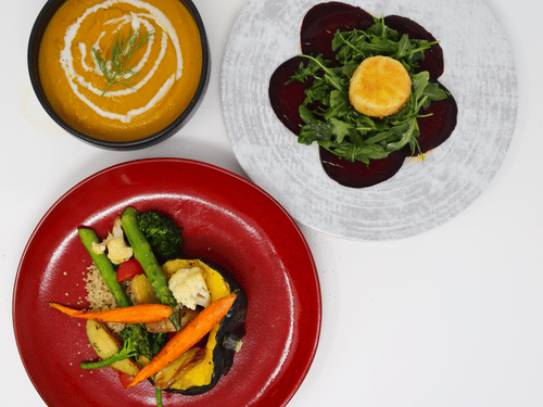 A colorful vegetarian meal at YO1 Longevity & Health Resorts featuring carrot soup, beetroot salad with greens, and a vegetable medley on a red plate
