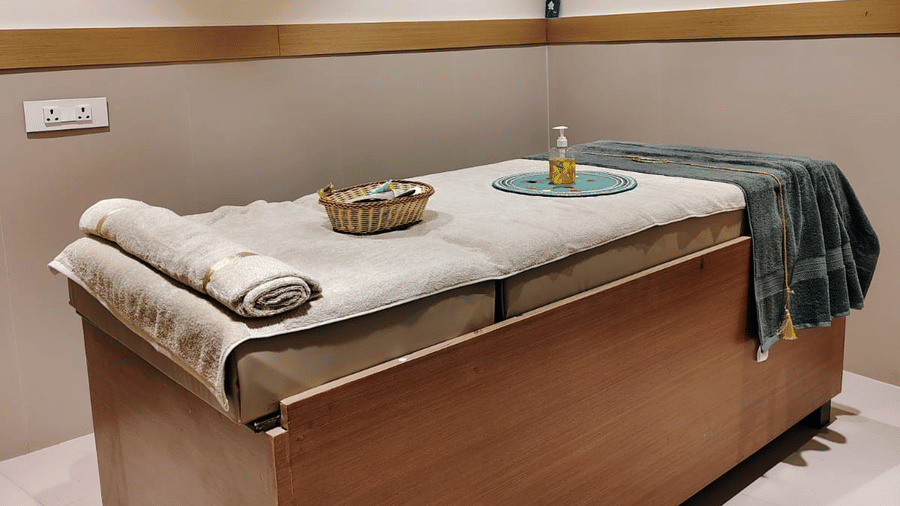 A spa room at ABN Sarovar Portico, Jim Corbett featuring a air-conditioner, a comfortable, high-raise bed which has a pillow, a basket with spa products, and a bottle of massage oil on it.