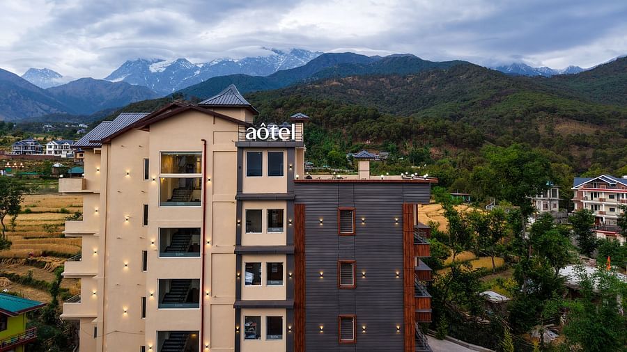 Facade of Aotel Palampur with a backdrop of majestic mountains under a cloudy sky