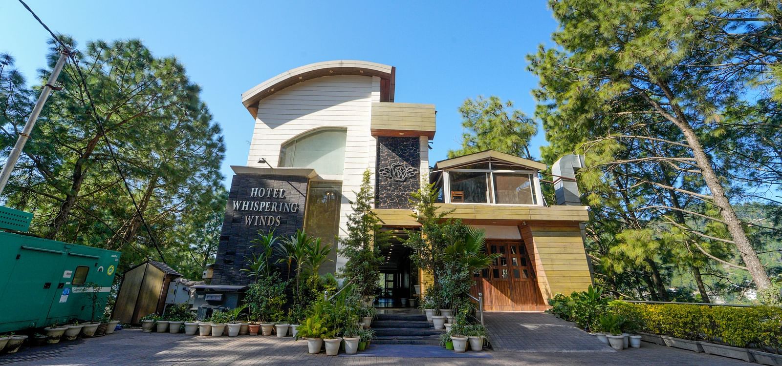 A facade image of DLS Whispering Winds surrounded by trees with a clear blue sky in the background