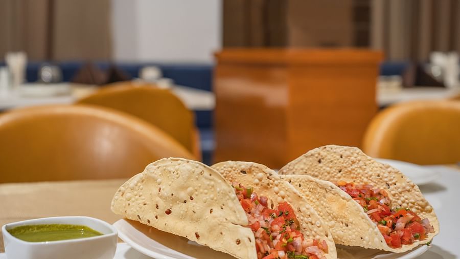 Three crispy shells filled with a vibrant mixture are served on a plate with a small bowl of green sauce