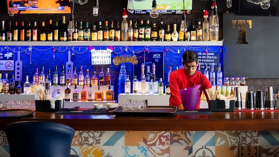 A bartender making a drink behind a brightly lit bar. The bar is decorated for Christmas with lights and garland.