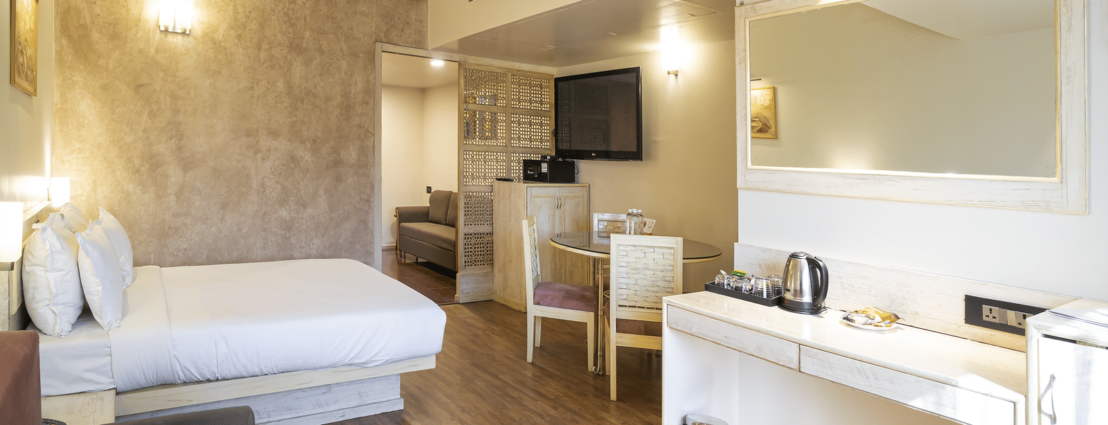 A suite with king size bed, dining table & chairs, television and wooden furniture at Infiniti Hotel, Indore.
