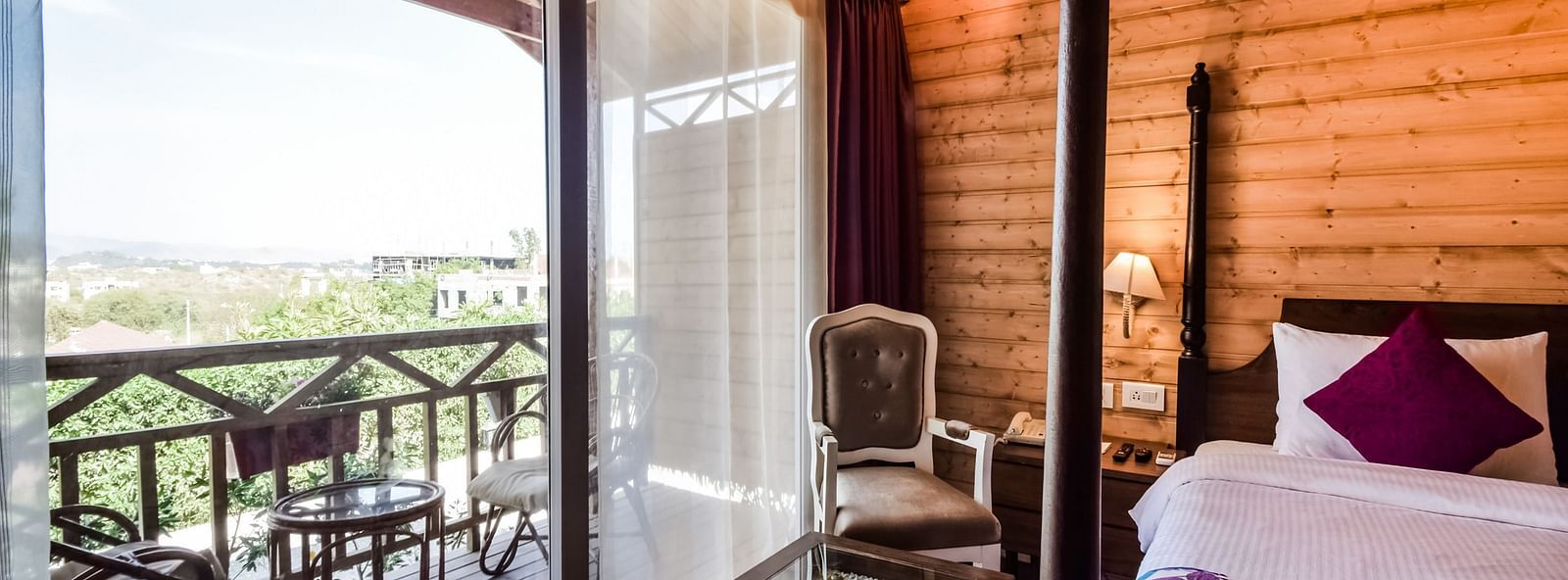  A cosy hotel room with wooden walls, a bed, and a balcony overlooking a scenic view. - Bamboo Saa Resort & Spa, Udaipur