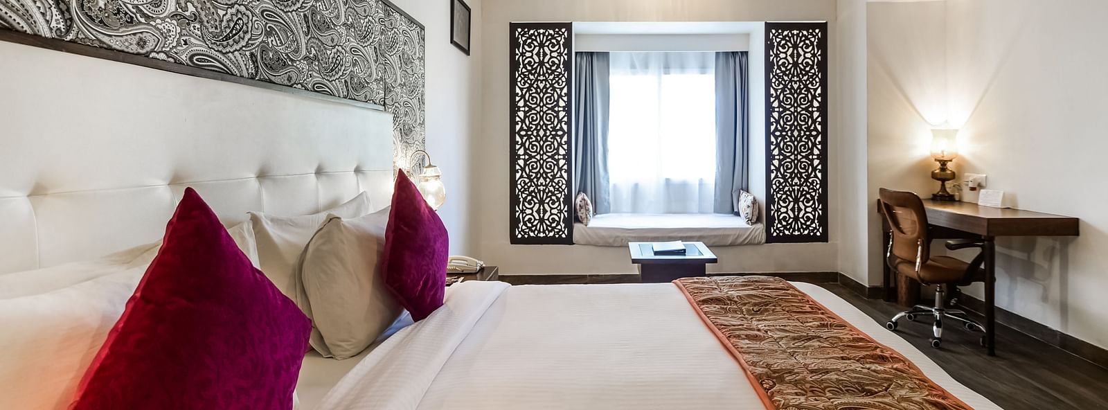  A hotel room with a large bed, a window seat, a desk, and decorative walls.- Bamboo Saa Resort & Spa, Udaipur