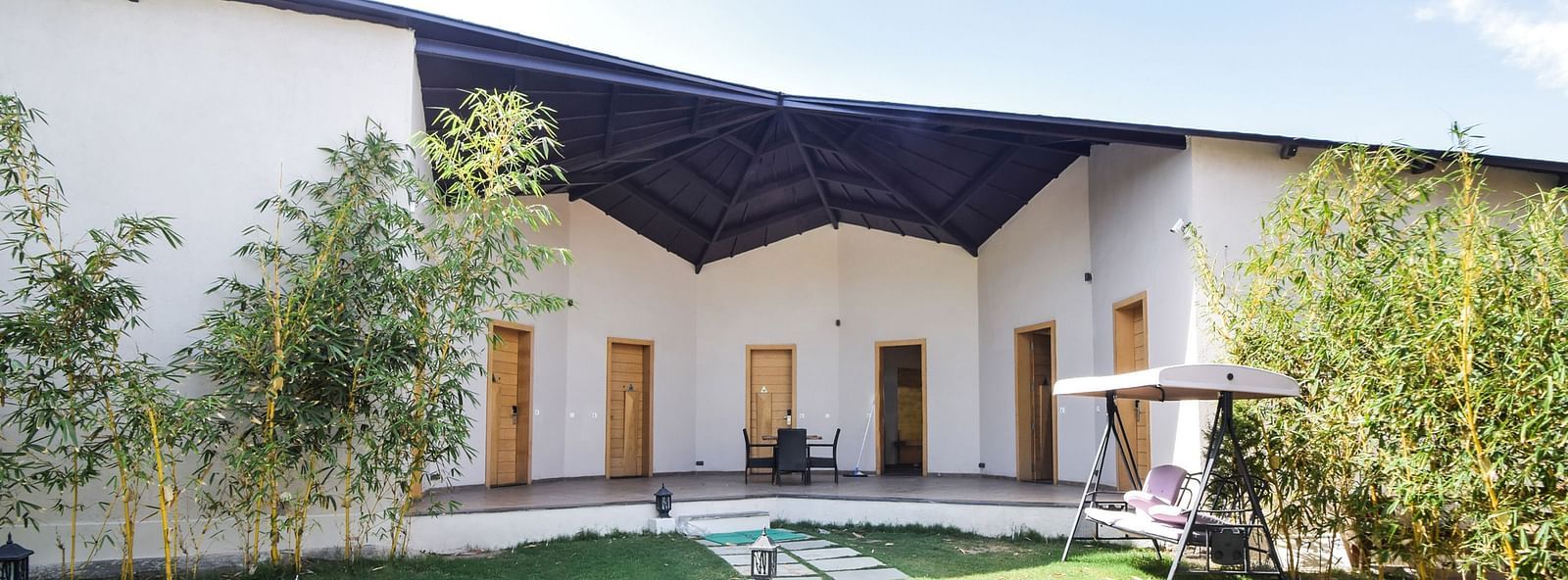 A building with a dark awning overlooks a grassy courtyard with a stone pathway. - Bamboo Saa Resort & Spa, Udaipur